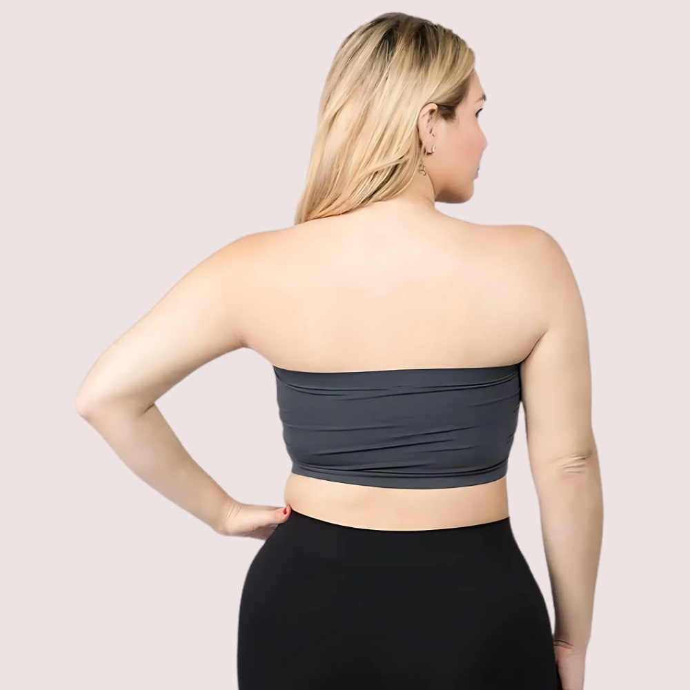 Woman wearing a dark gray tube top and black leggings on a light pink background