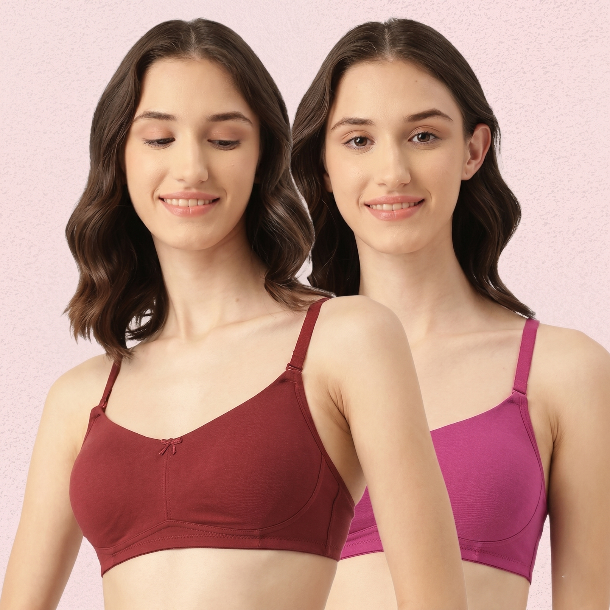 Two women wearing different colored bras against a pink background