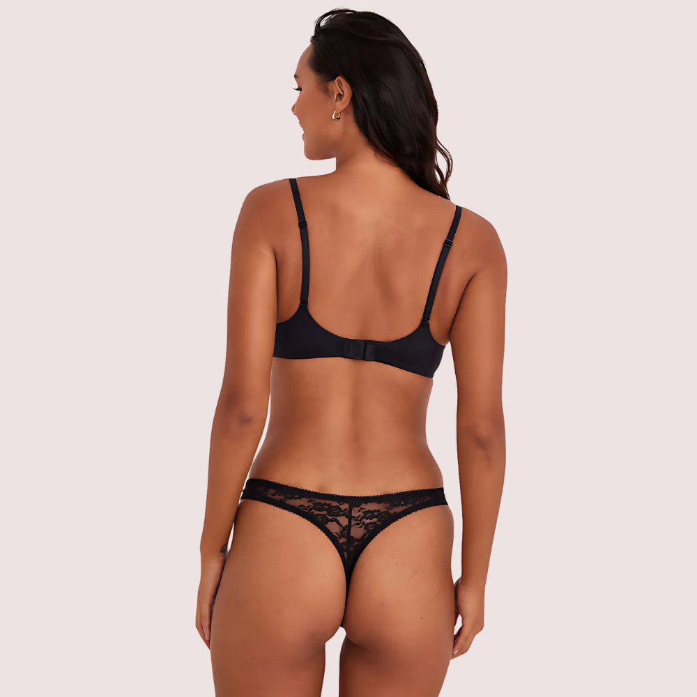 Woman wearing a black lace lingerie set on a light pink background