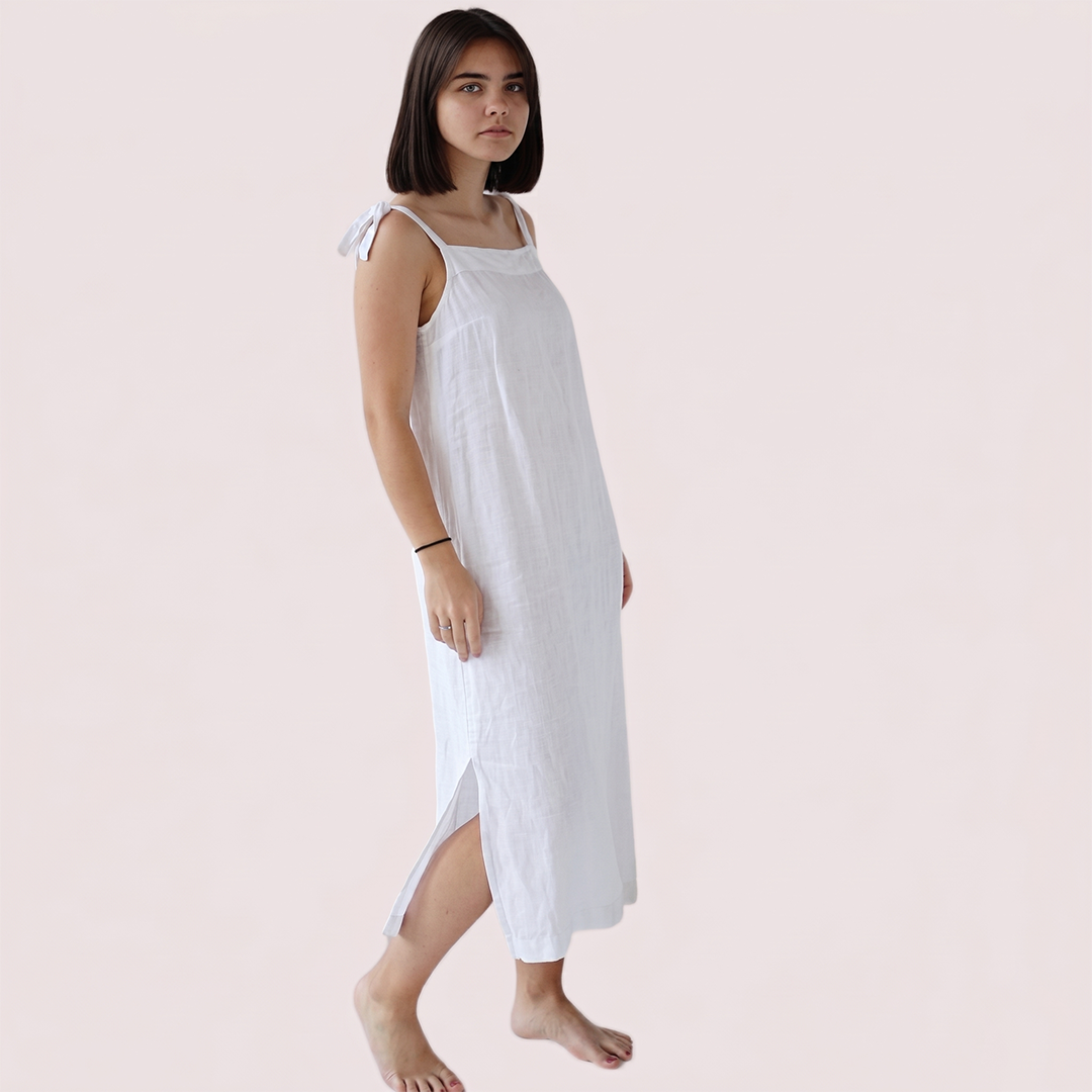 Woman wearing a white sleeveless dress with a bow on a plain background
