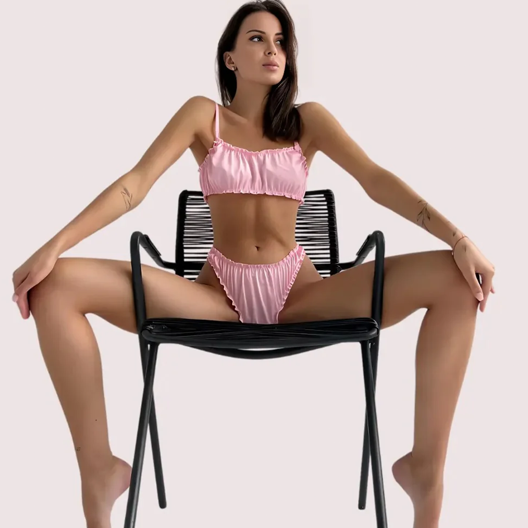 Woman in a pink bikini sitting on a black chair against a light pink background