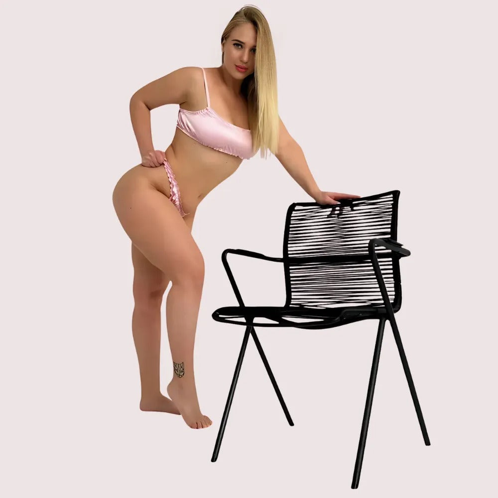 Woman in pink bikini sitting next to a black chair on a plain background