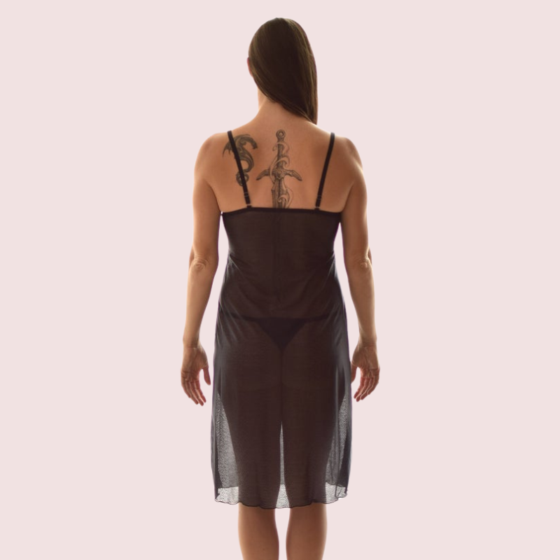 Woman wearing a sheer black dress with visible tattoos on a plain background