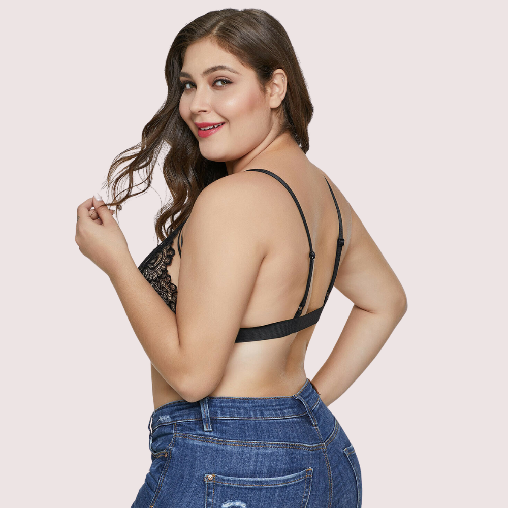 Woman wearing a black lace bralette and blue jeans on a light pink background