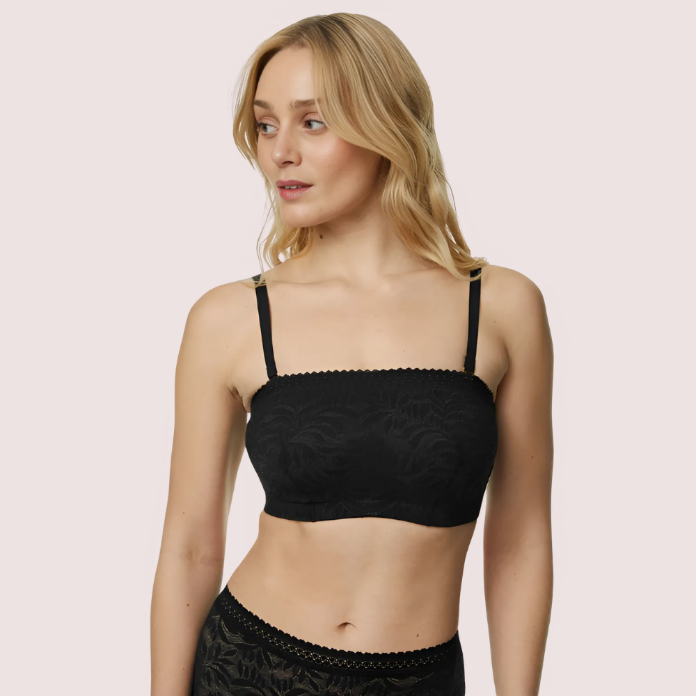 Woman wearing a black lace bralette against a light pink background