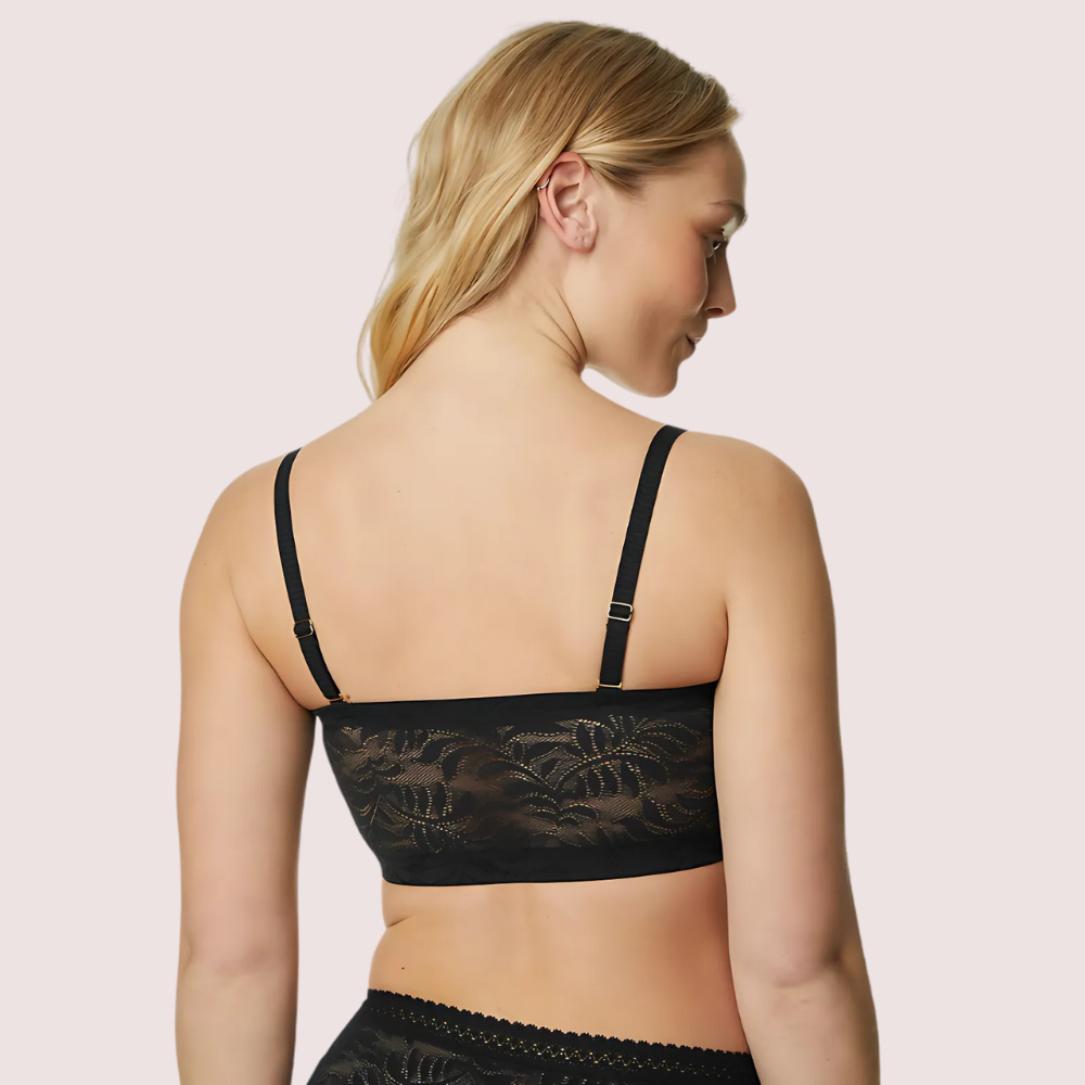 Woman wearing a black lace bralette on a light pink background