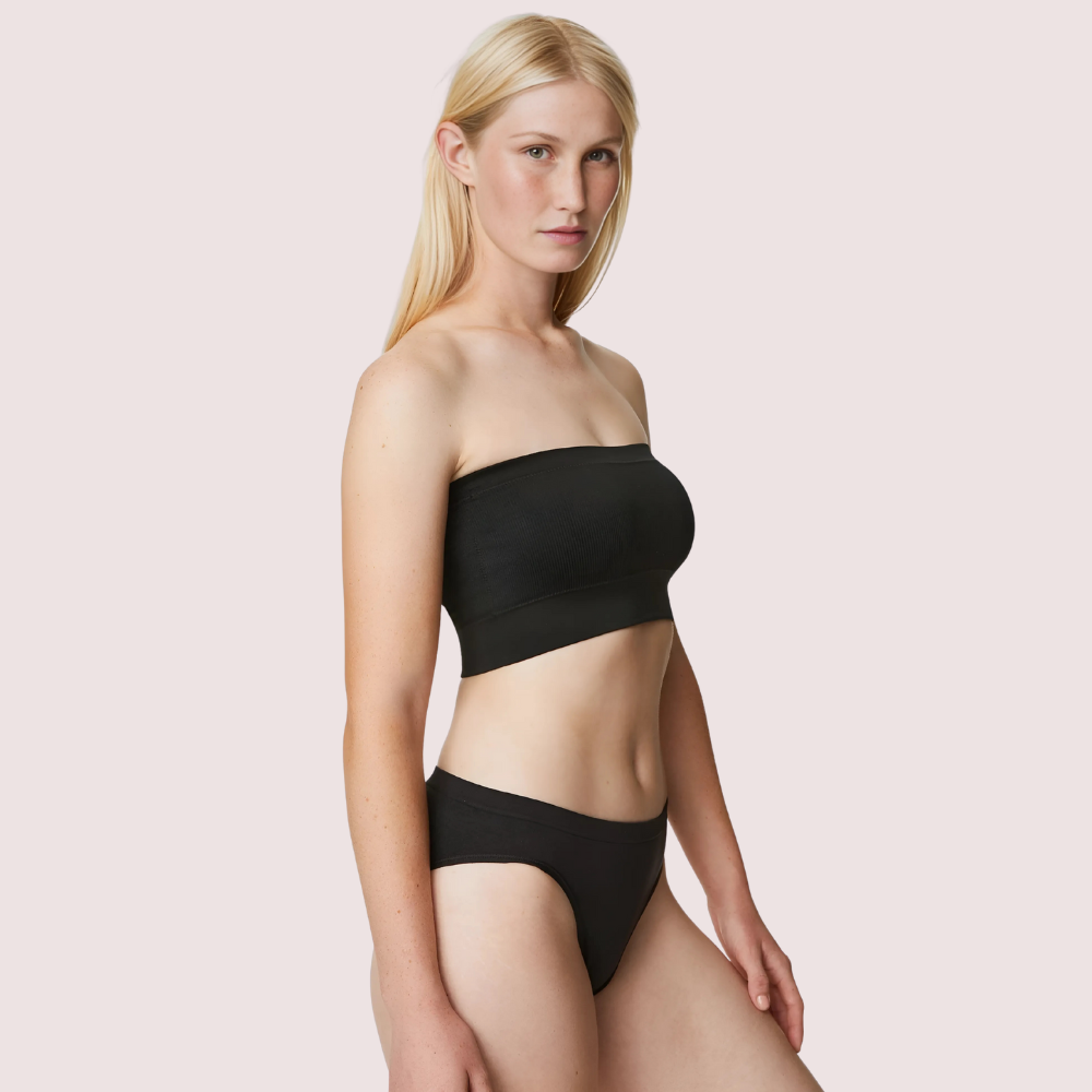 Woman wearing a black strapless top and high-waisted bikini bottom on a light pink background