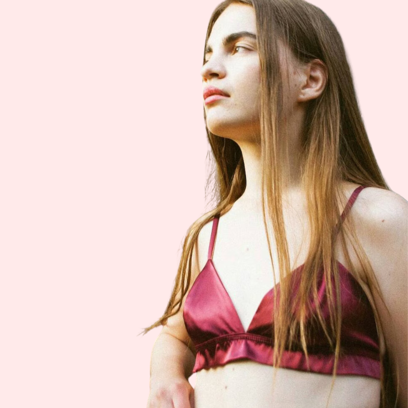Woman wearing a pink satin bralette against a light pink background