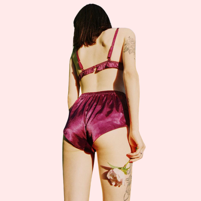 Person wearing a burgundy satin lingerie set on a light pink background