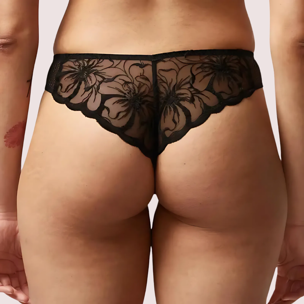 Black lace underwear being worn by a person on a plain background