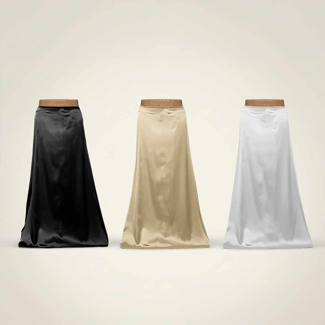 Three satin skirts in black, beige, and white on mannequins against a plain background.