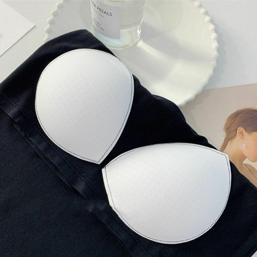 White adhesive bra pads on a black fabric background with a glass of water and a magazine in the background.