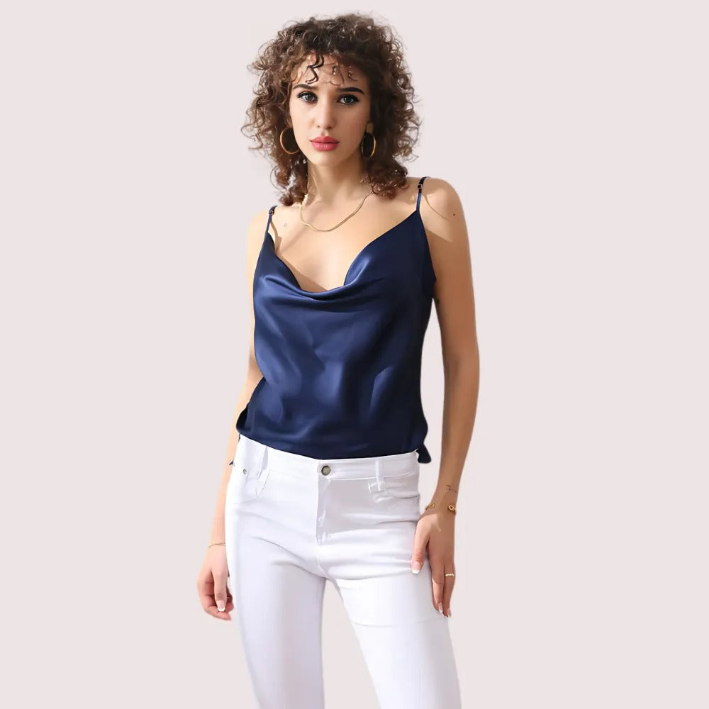 Woman wearing a navy blue satin top and white pants on a plain background