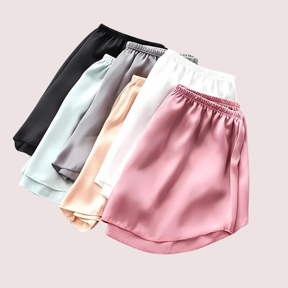 Five satin shorts in black, gray, white, beige, and pink on a light pink background.