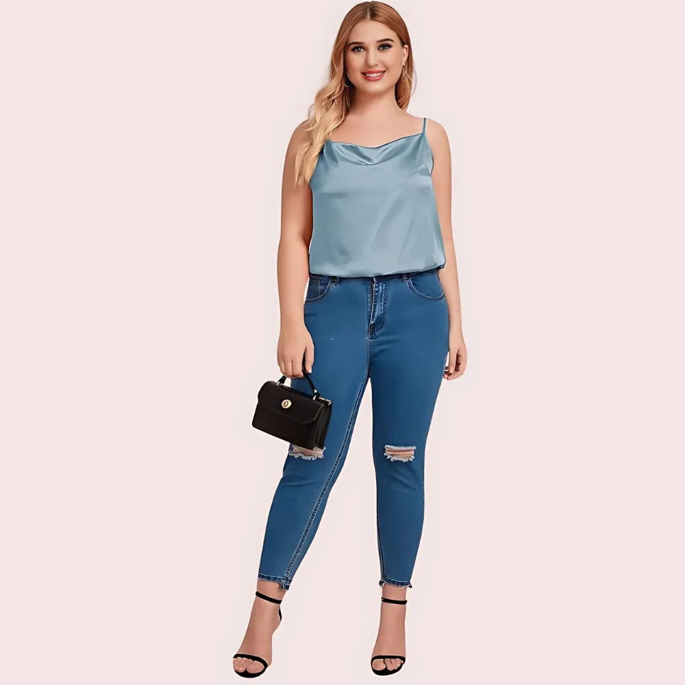 Woman wearing a light blue top and blue jeans holding a black handbag on a pink background