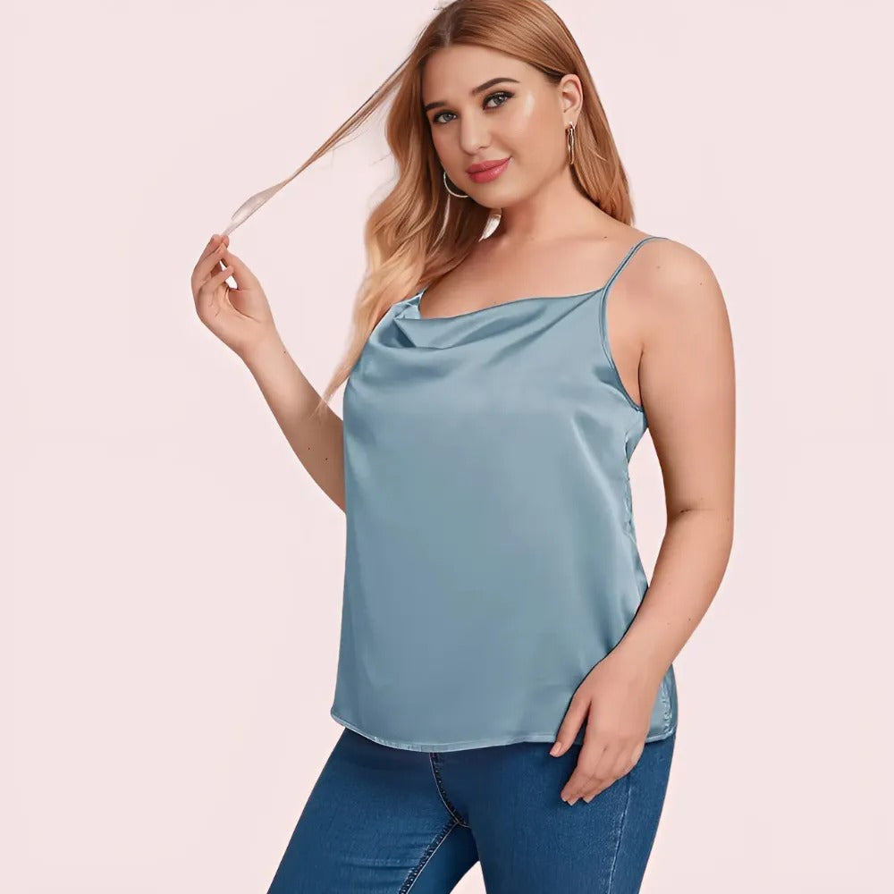 Woman wearing a blue satin tank top and jeans on a pink background