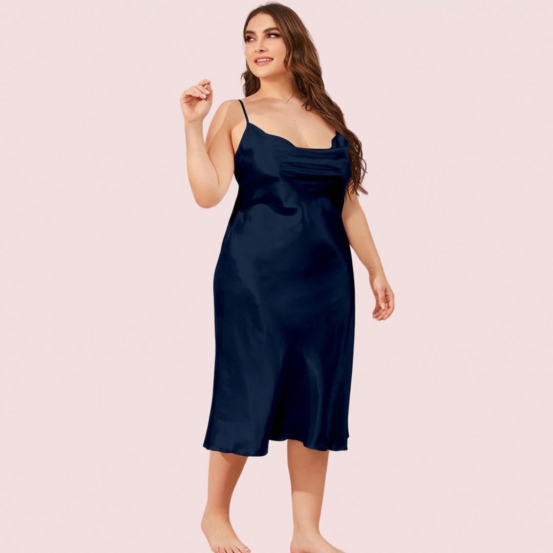Woman wearing a navy blue satin slip dress on a light pink background