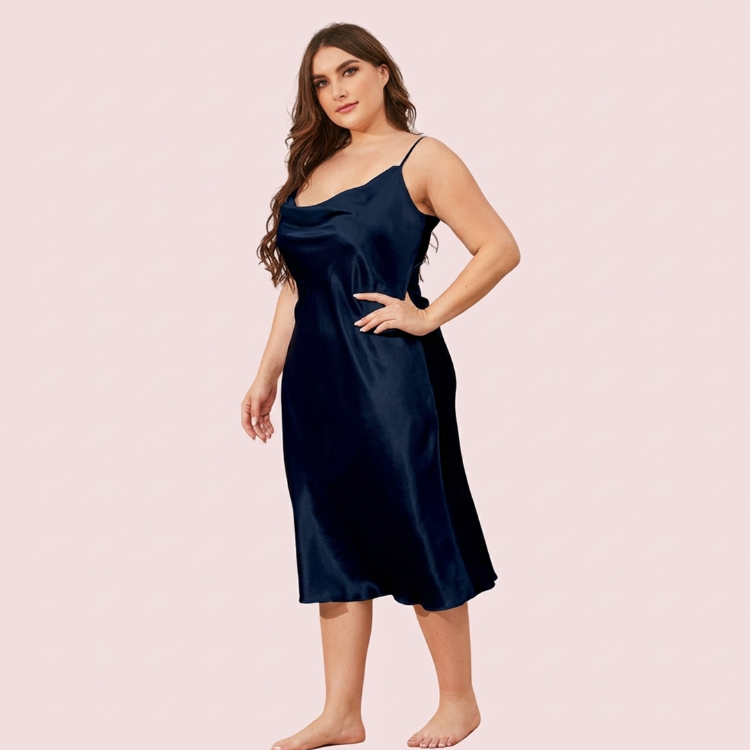 Woman wearing a navy satin slip dress on a pink background