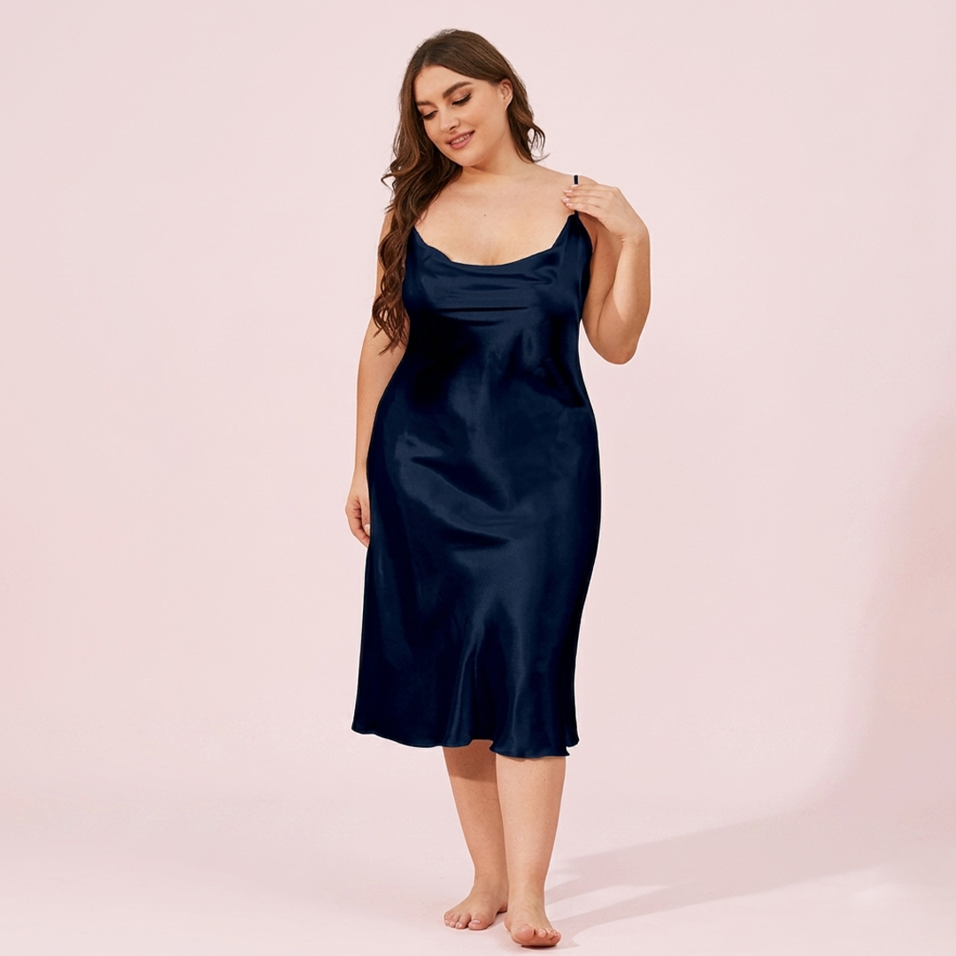 Woman wearing a navy satin slip dress against a pink background