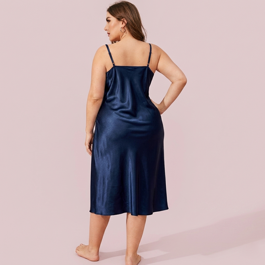 Woman wearing a navy satin slip dress against a light pink background
