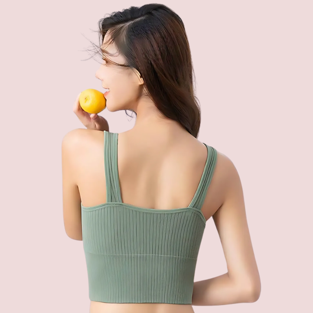 Woman wearing a green sports bra holding an orange against a light pink background