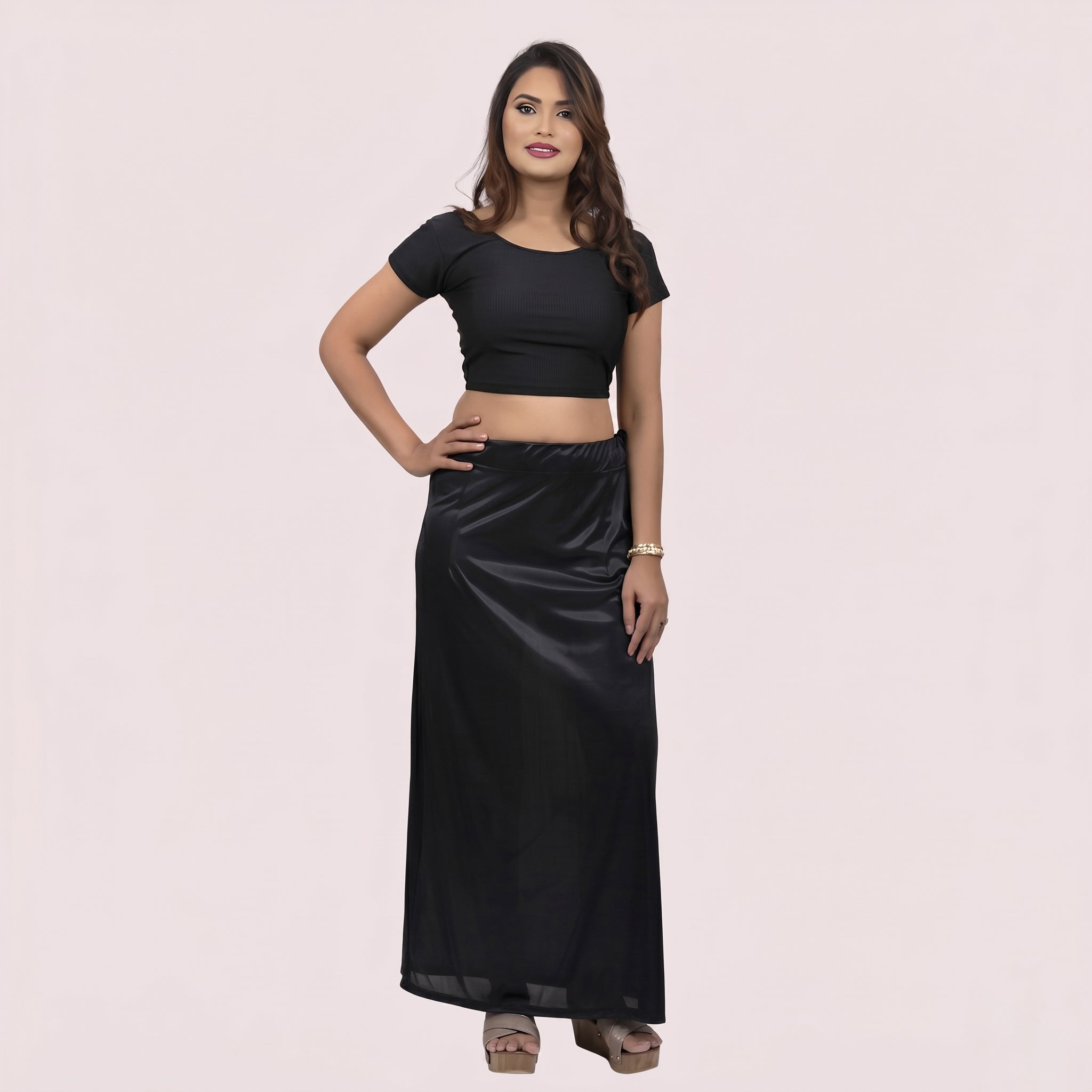Woman wearing a black crop top and long black skirt on a light pink background