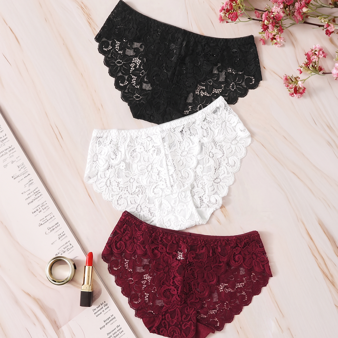 Black, white, and burgundy lace panties on a light pink surface with flowers and a ring.