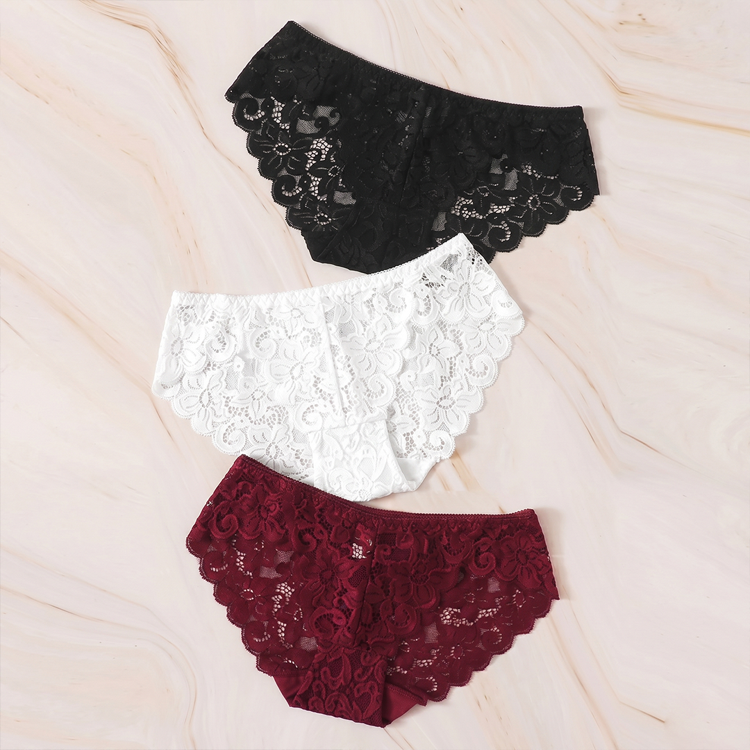 Three pairs of lace underwear in black, white, and burgundy on a beige fabric background.