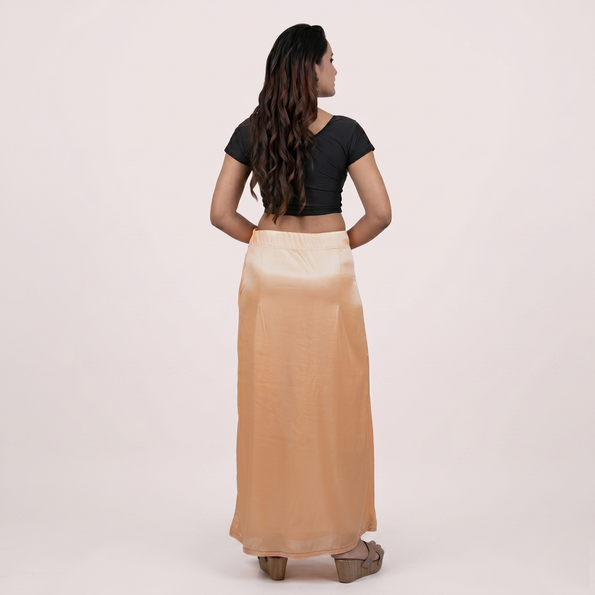 Woman wearing a black top and beige skirt on a light pink background