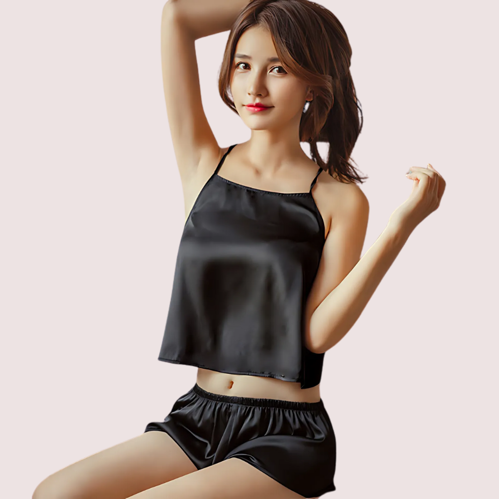 Woman wearing a black satin camisole and shorts on a light pink background
