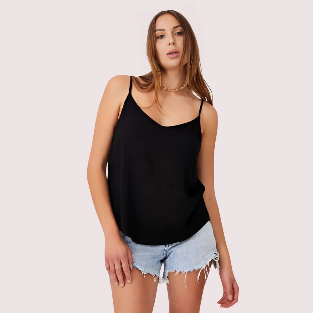 Woman wearing a black tank top and denim shorts on a light pink background