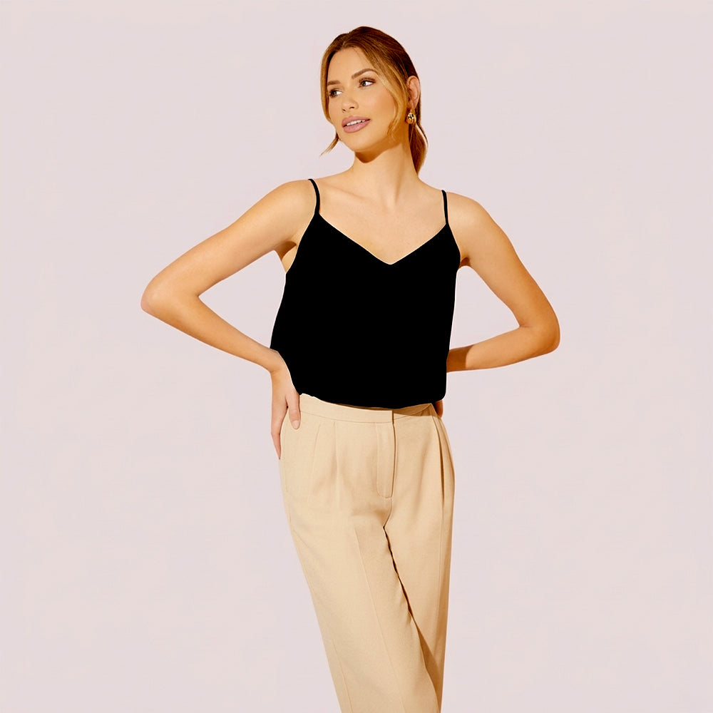 Woman wearing a black top and beige pants on a light pink background