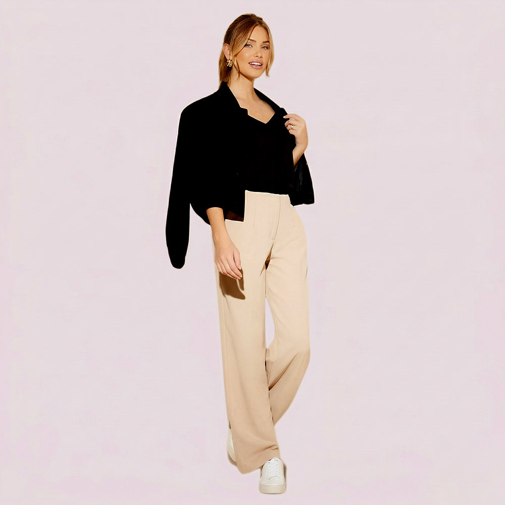 Woman wearing a black top and beige pants on a light pink background