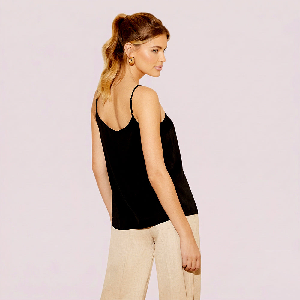 Woman wearing a black tank top and beige pants on a light pink background