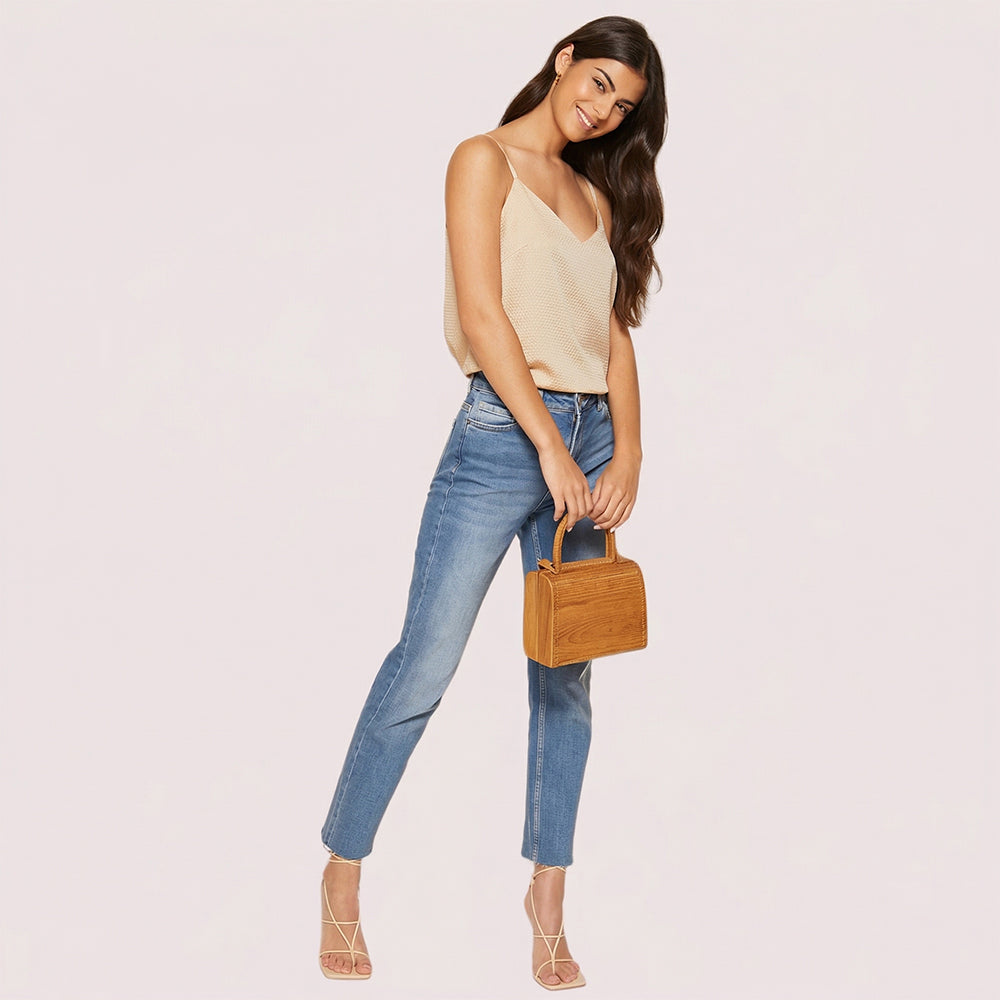 Woman holding a brown handbag against a light pink background