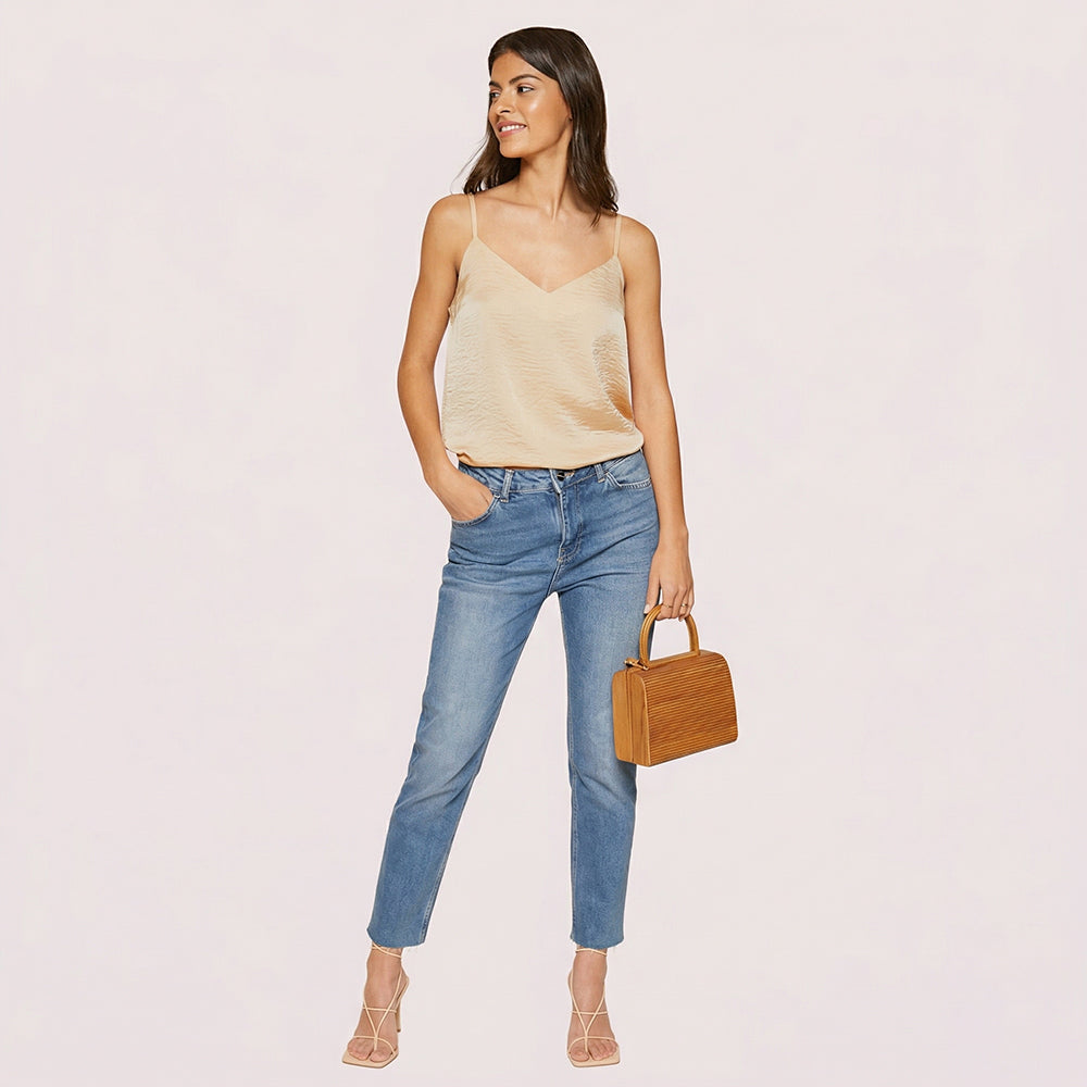 Woman wearing a beige top and blue jeans, holding a brown handbag on a light pink background