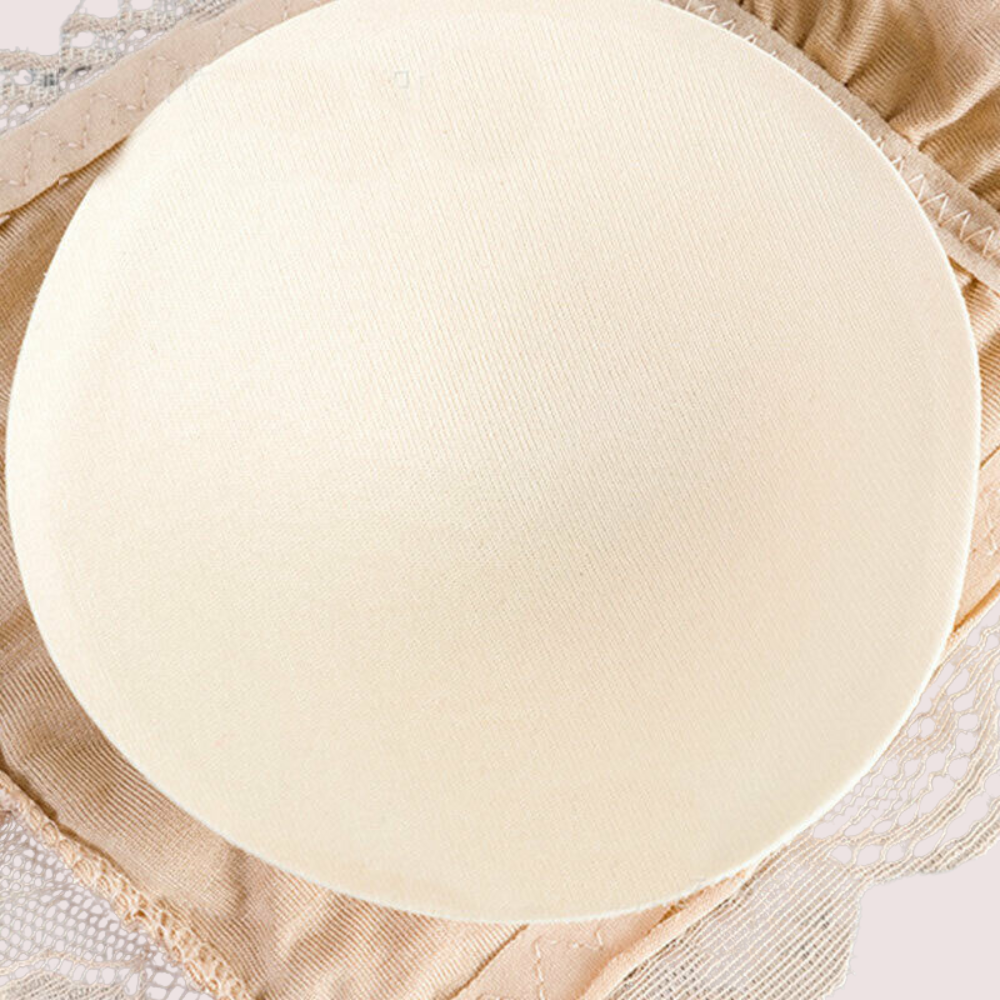 Beige bralette with a round white object on top, placed on a textured beige surface.