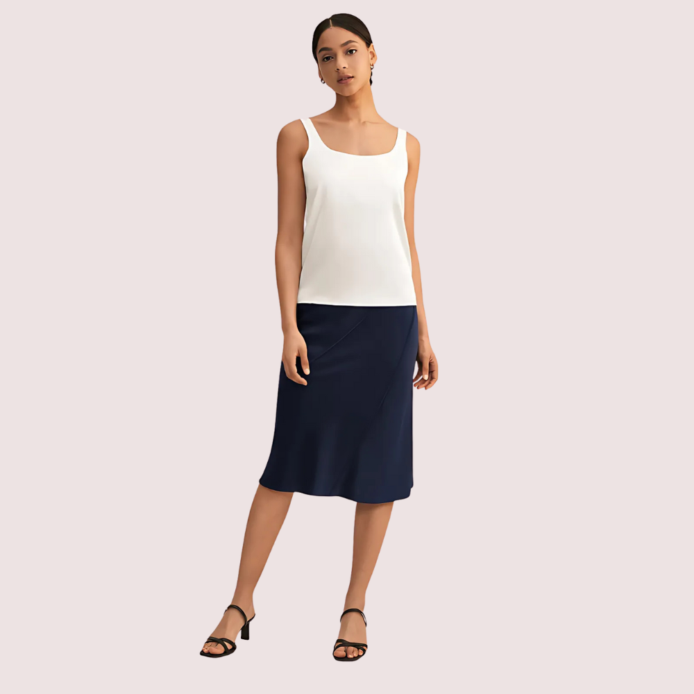 Woman wearing a white sleeveless top and navy skirt on a light pink background