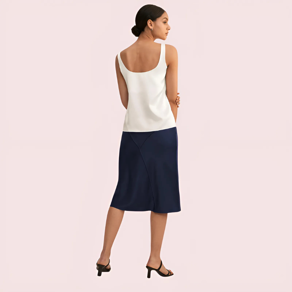 Woman wearing a white top and navy skirt on a light pink background