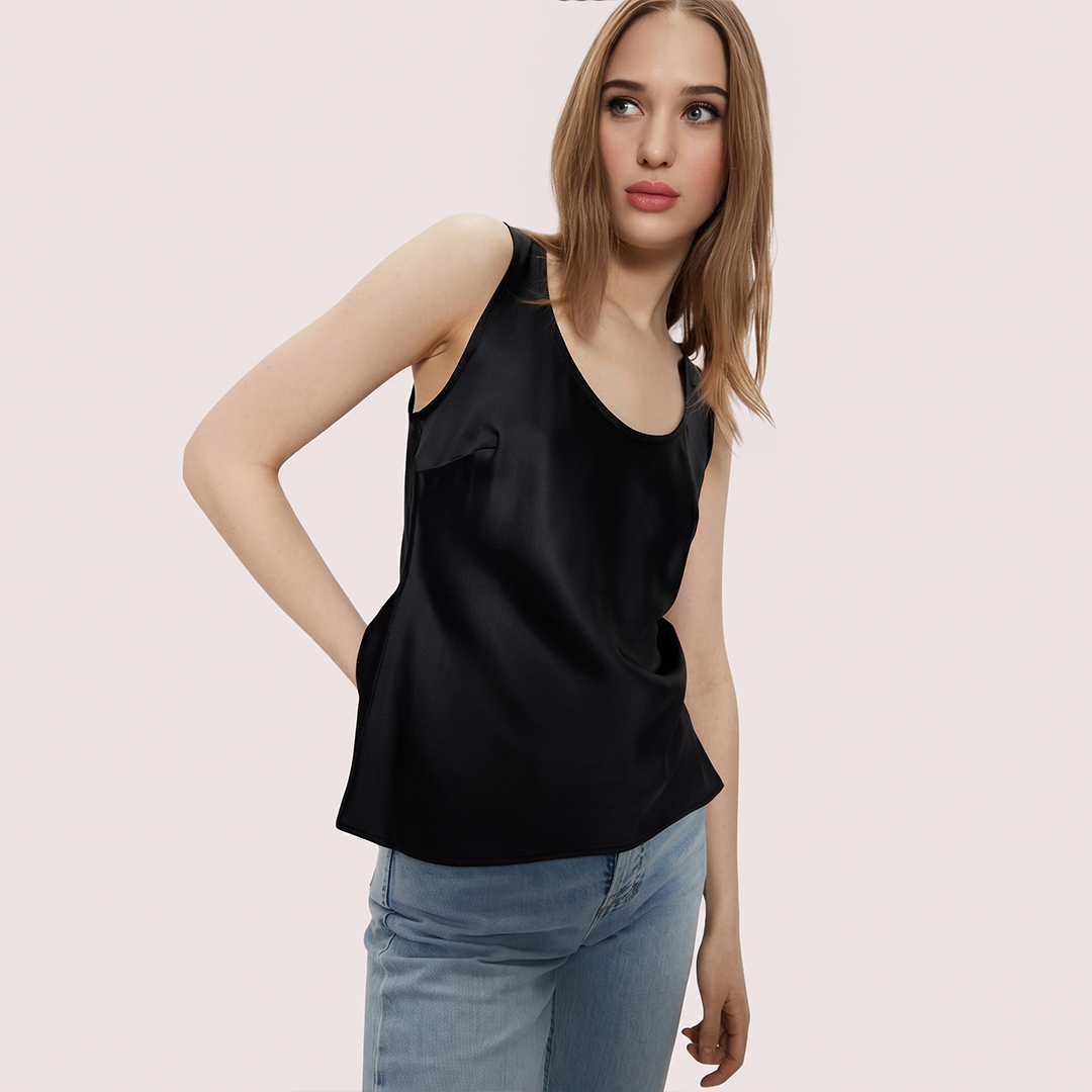 Woman wearing a black sleeveless top and light blue jeans on a pink background