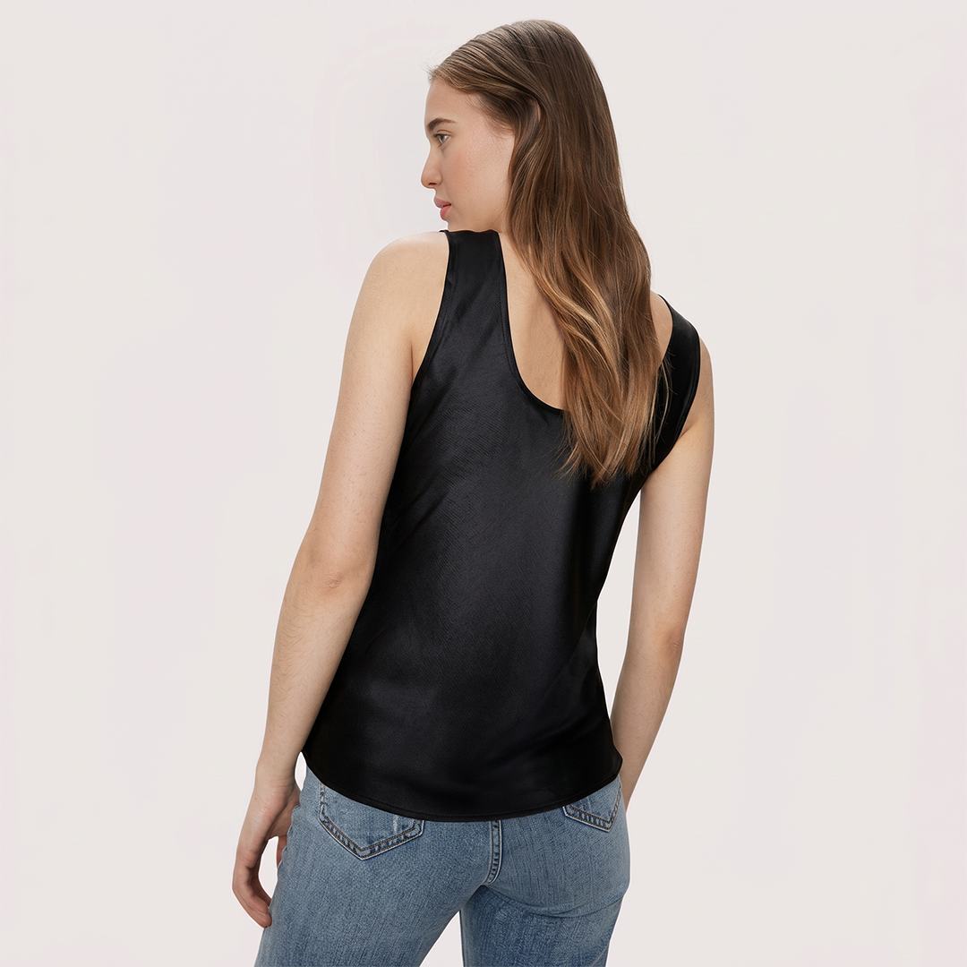Woman wearing a black sleeveless top and blue jeans on a light pink background