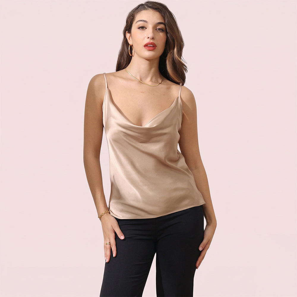 Woman wearing a beige satin camisole and black pants on a light pink background