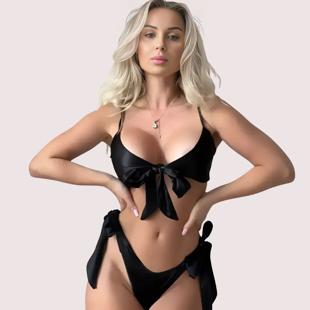 Woman wearing a black bikini with a bow design on a plain background