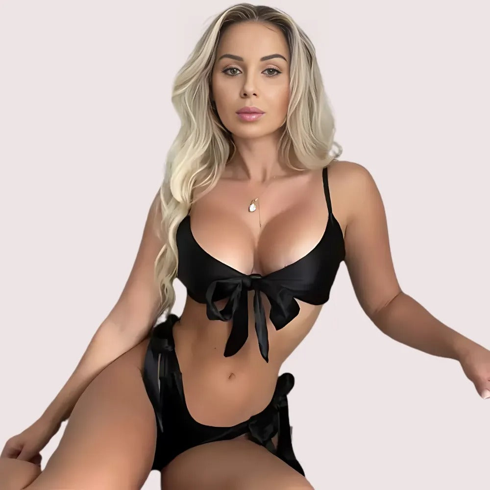 Woman wearing a black bikini with a bow design on a plain background
