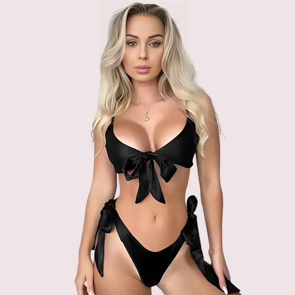 Woman wearing a black bikini with bow details on a light pink background